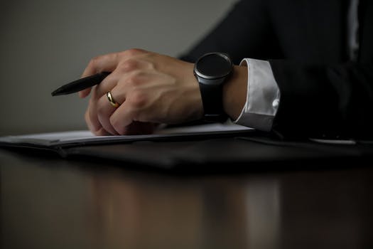 Close-up of a person writing with a pen, wearing a smartwatch and a wedding ring.